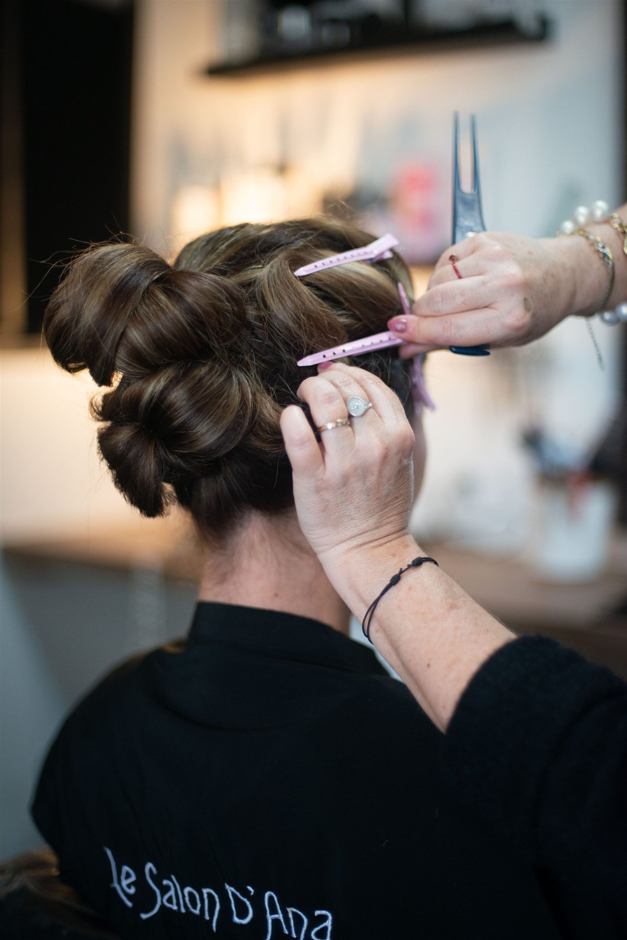 Vue de dos du chignon avec ciseaux et épingles — cape Le Salon D'Ana visible — finition coiffure mariage