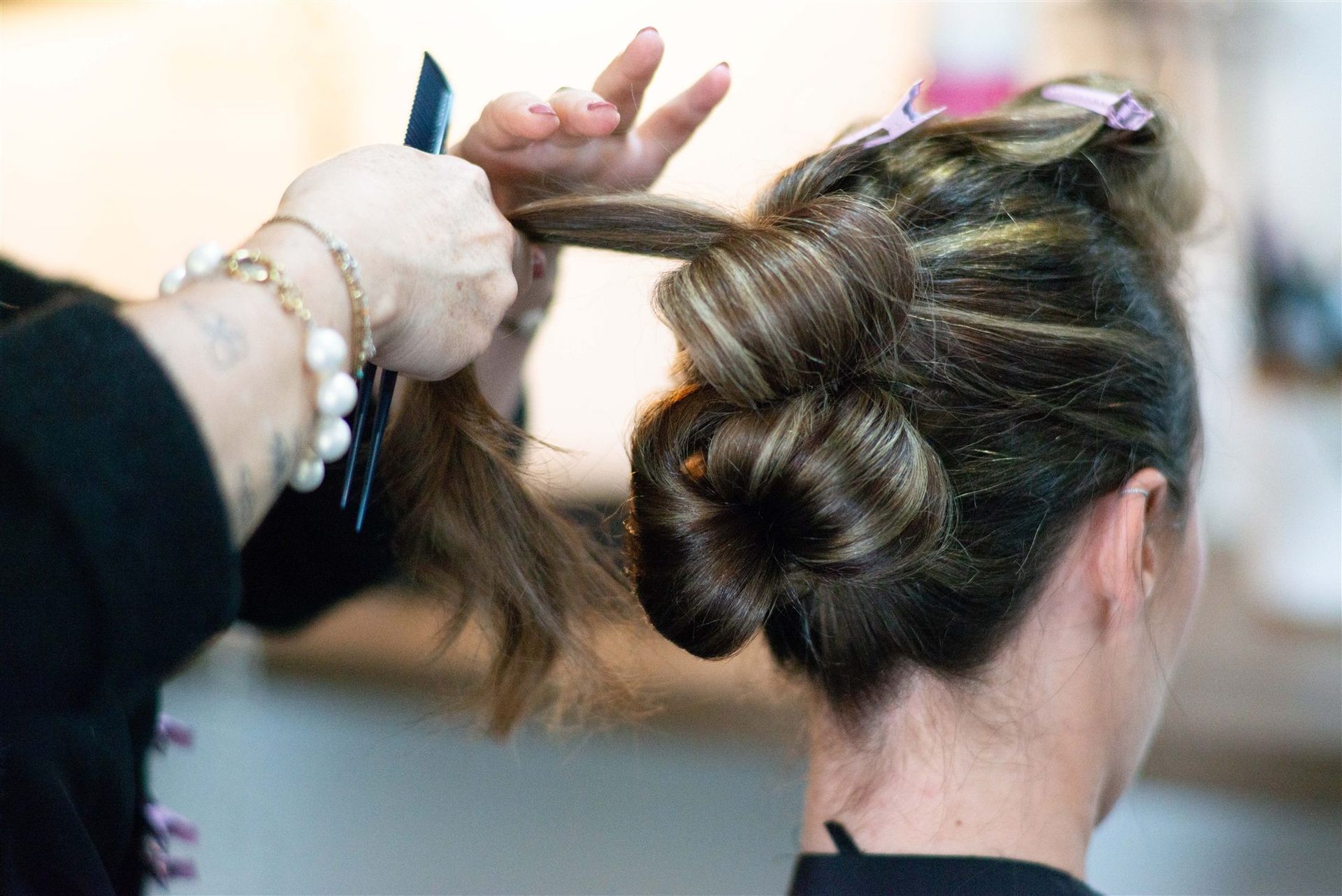 Vue de dos du chignon en cours de finalisation — mains d'Annabel et épingles roses — Salon D'Ana