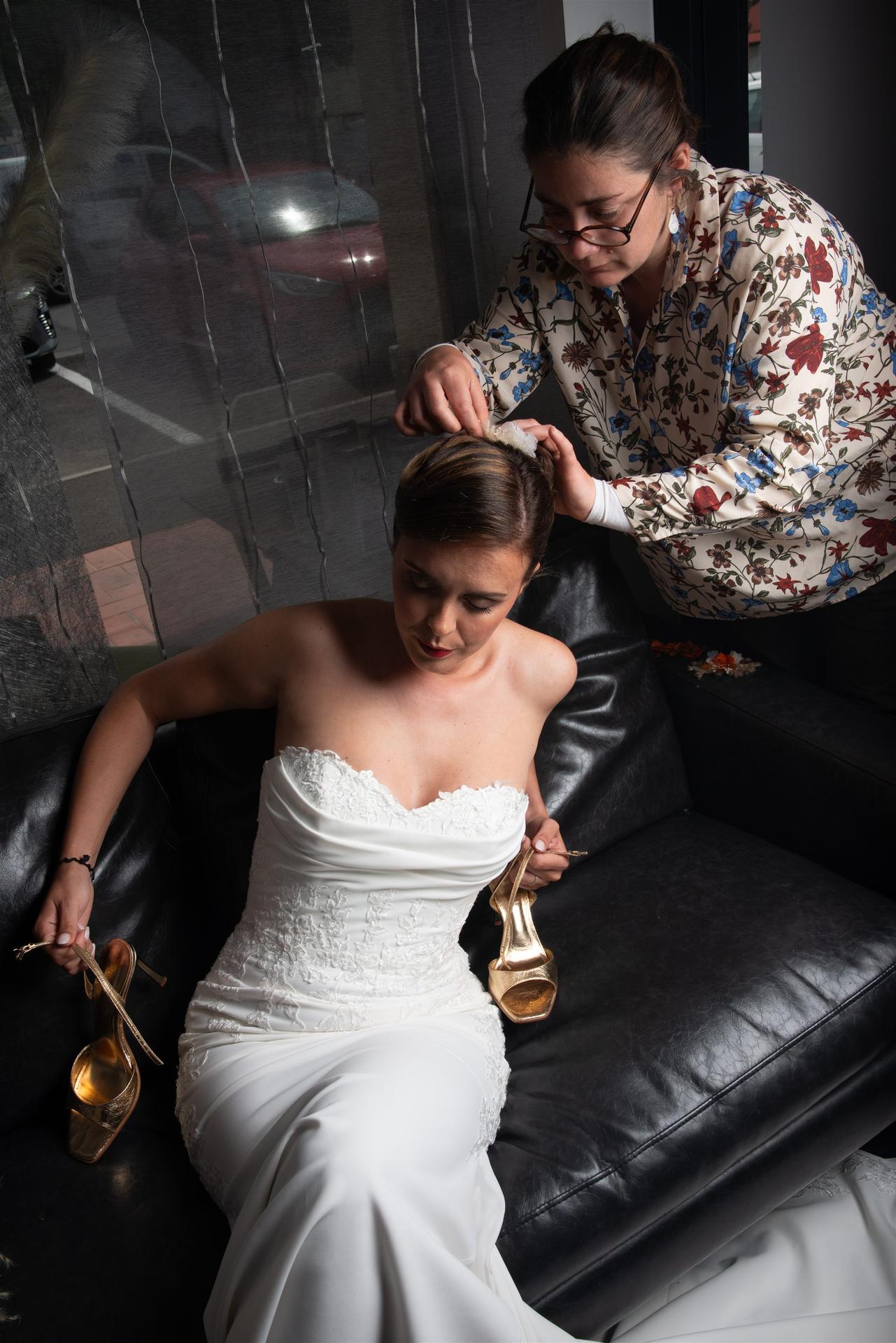 Annabel finalise la coiffure de la mariée assise sur un canapé noir, talons dorés en main — Salon D'Ana Perpignan